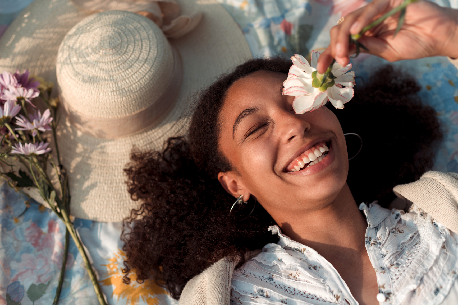 Portrait of a cute young woman holding a white flower over her eye and laughing